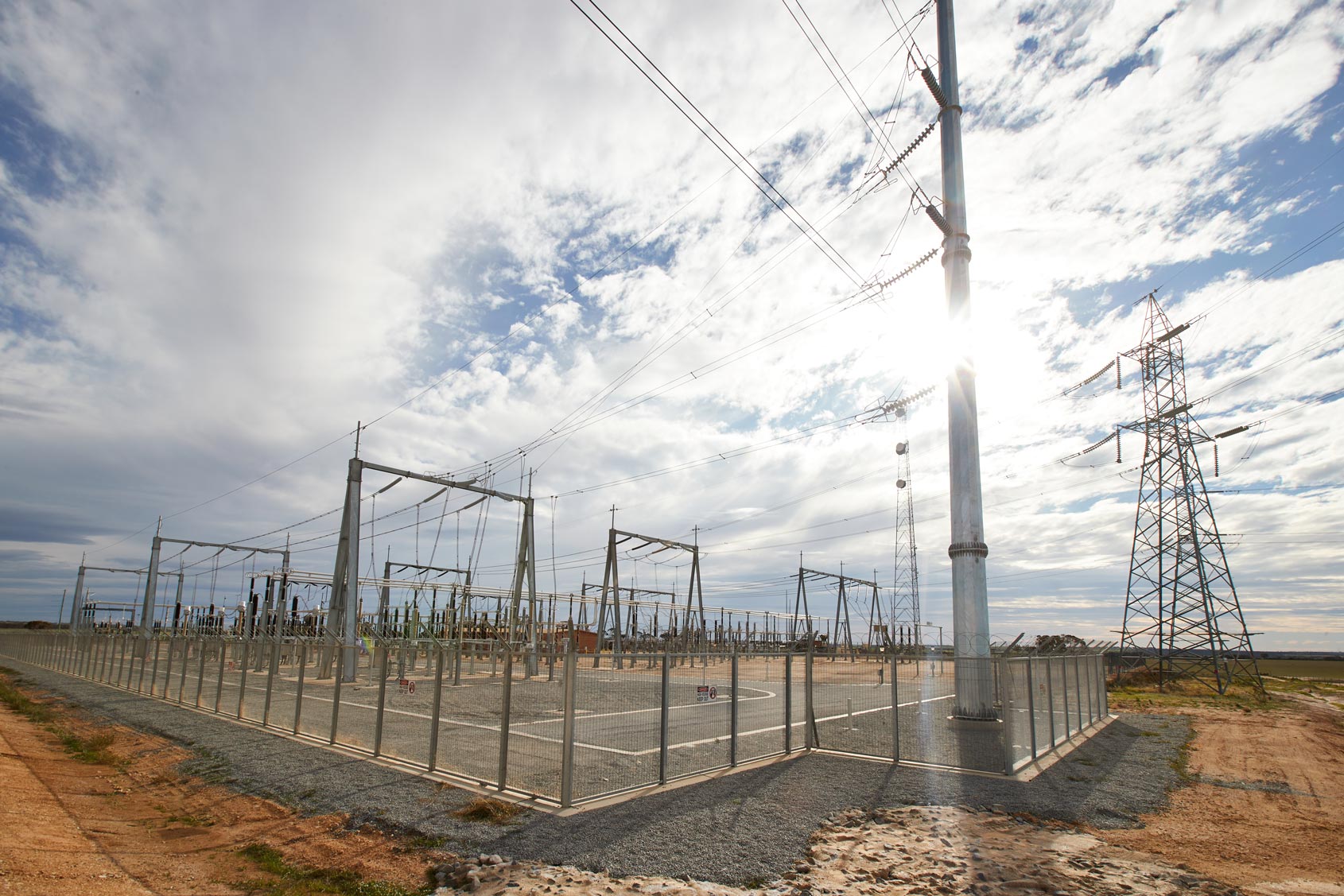 Electrical substation and transmission towers in Western Australia under a partly cloudy sky, supporting the power network.