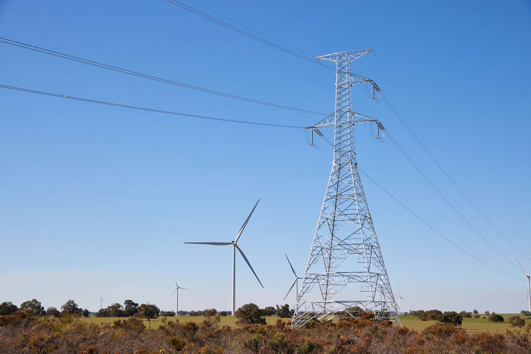 Transmission tower in a field with wind turbines in the background