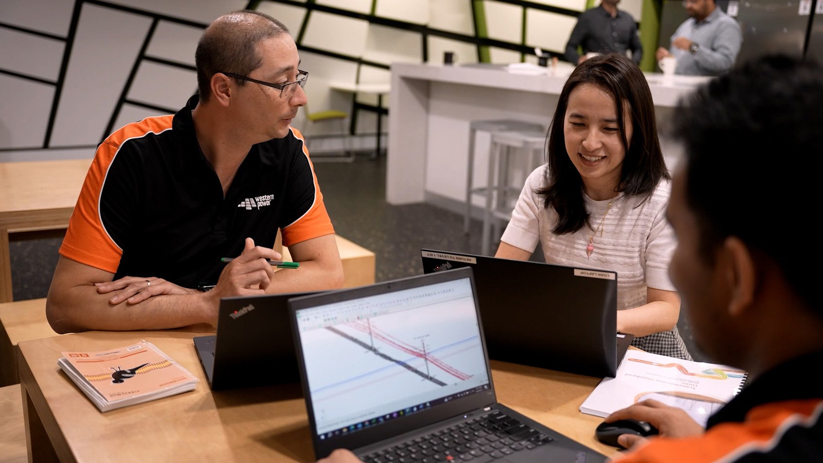 Three Western Power employees sat at a desk together looking at their laptop screens