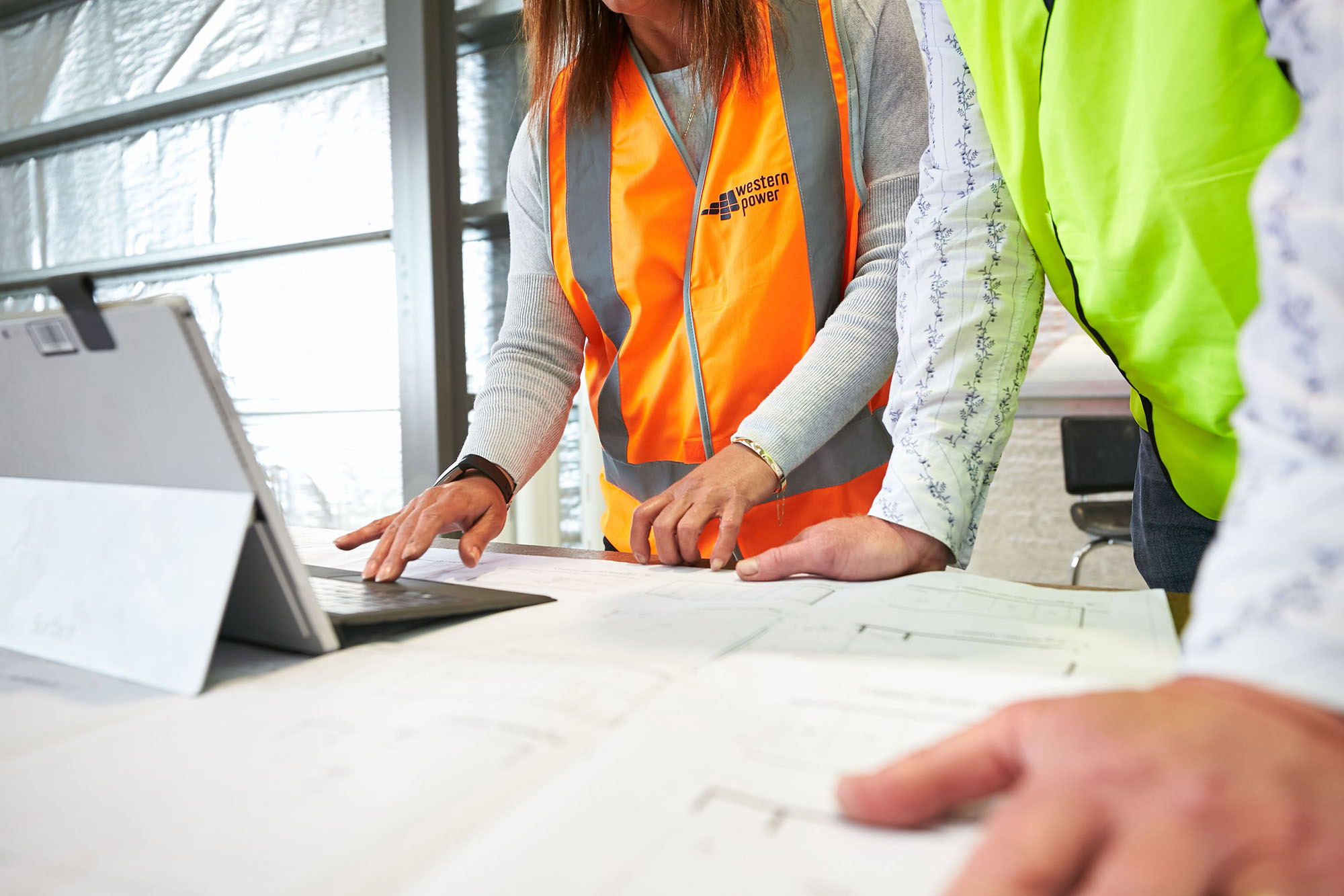 Two people wearing high-visibility safety vests standing at a table reviewing blueprints and architectural plans.