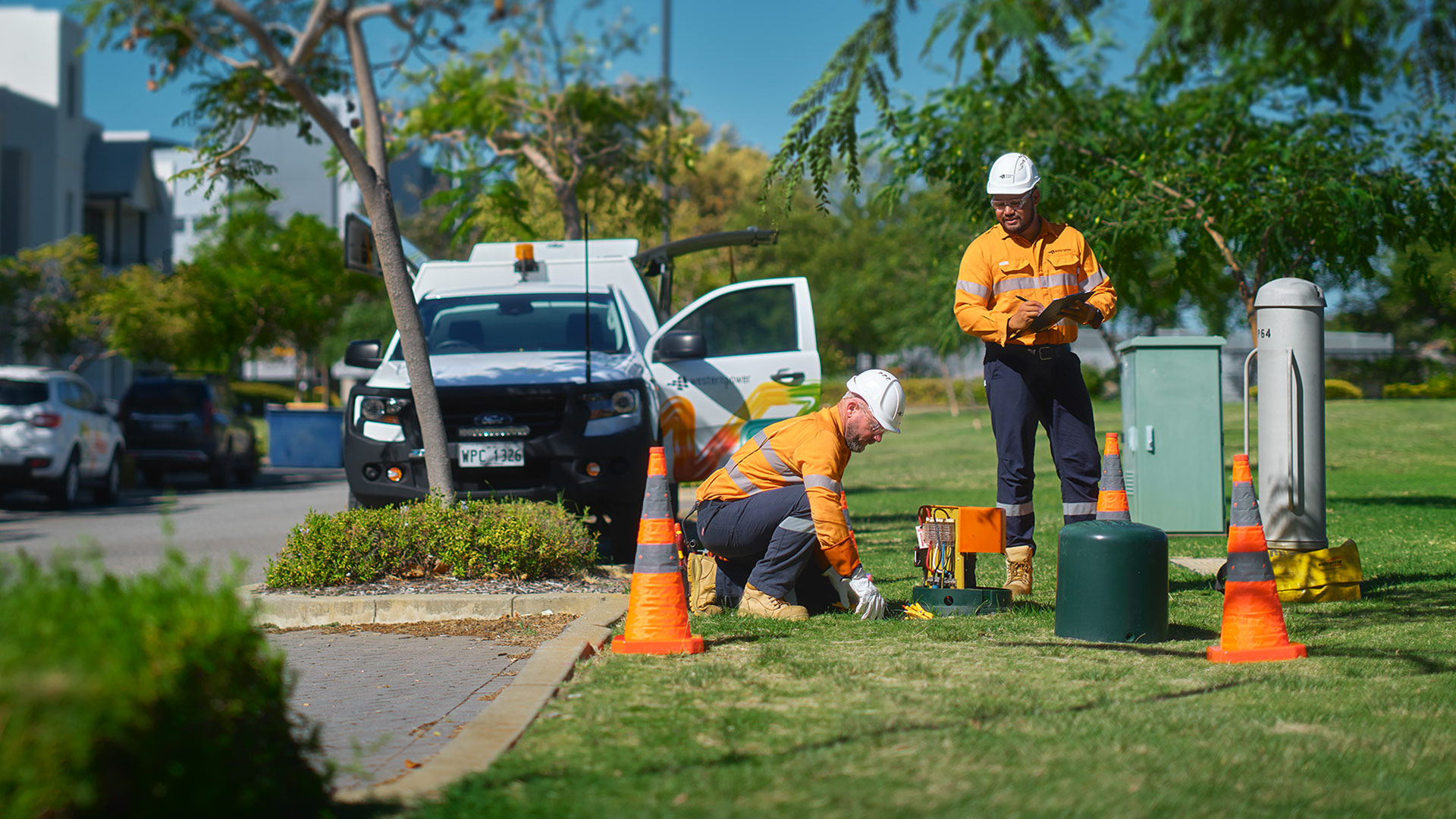 Western Power crew inspecting underground power infrastructure near a green dome in a suburban area.