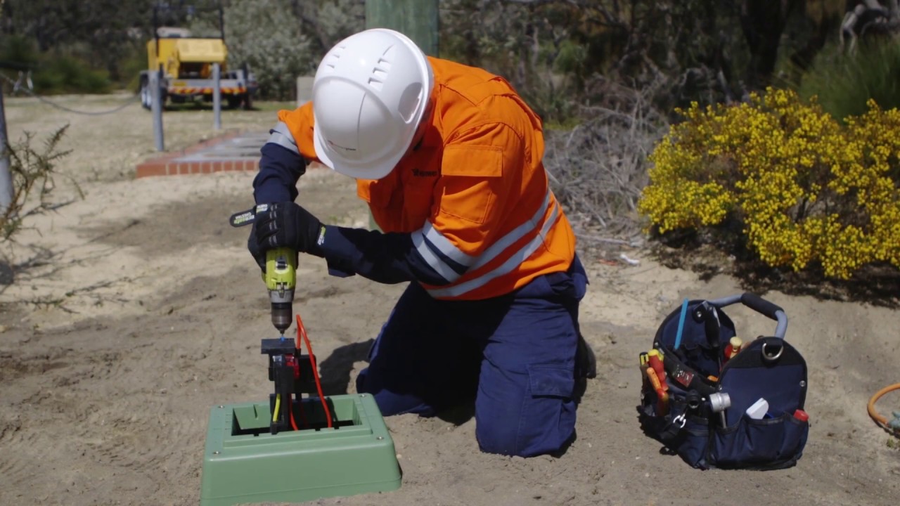 Two Western Power crew in safety gear performing maintenance on underground electrical equipment in a suburban area.