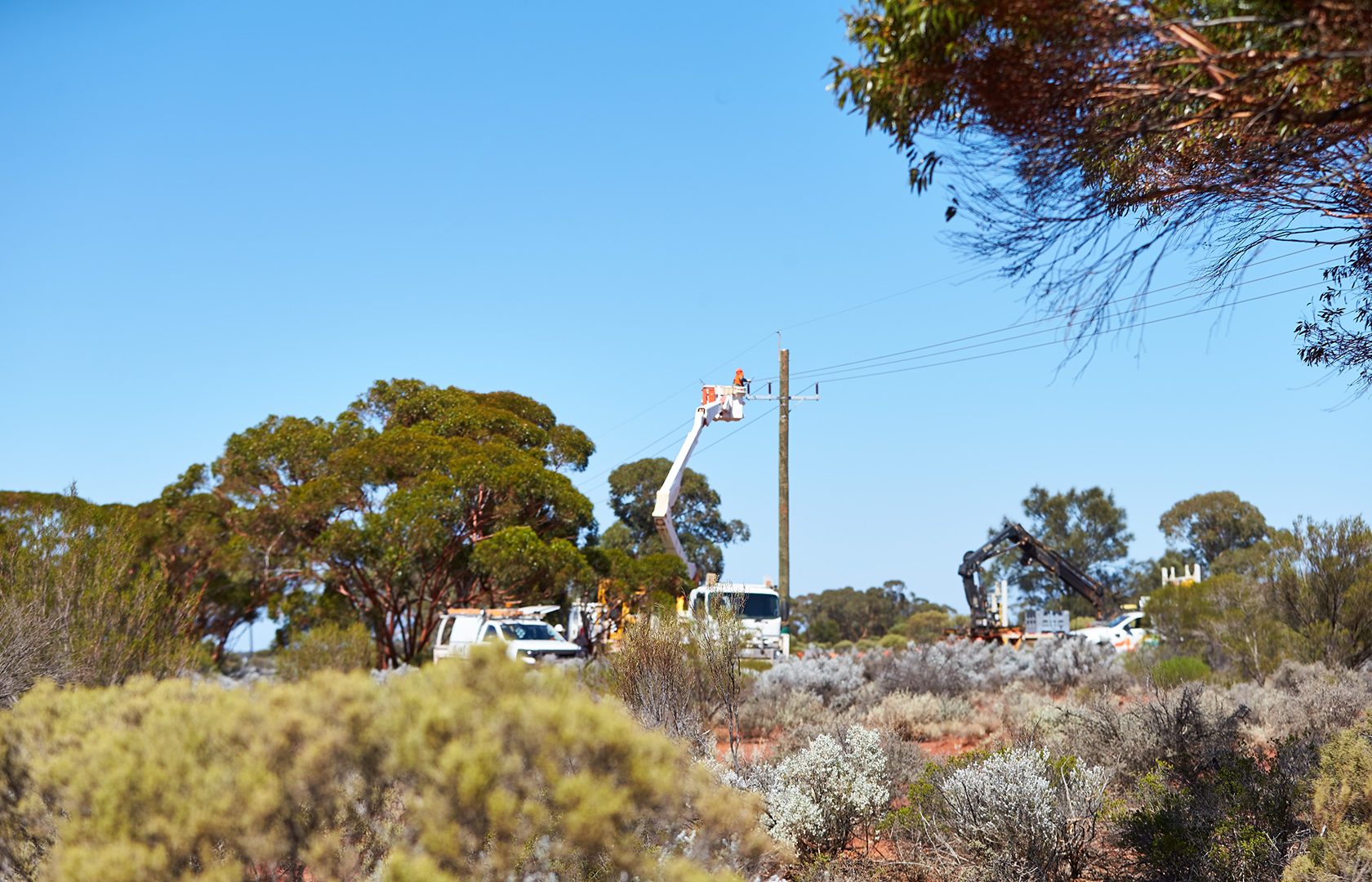 A wide shot of a field crew with an elevated work platform performing maintenance on a power pole in a rural area.