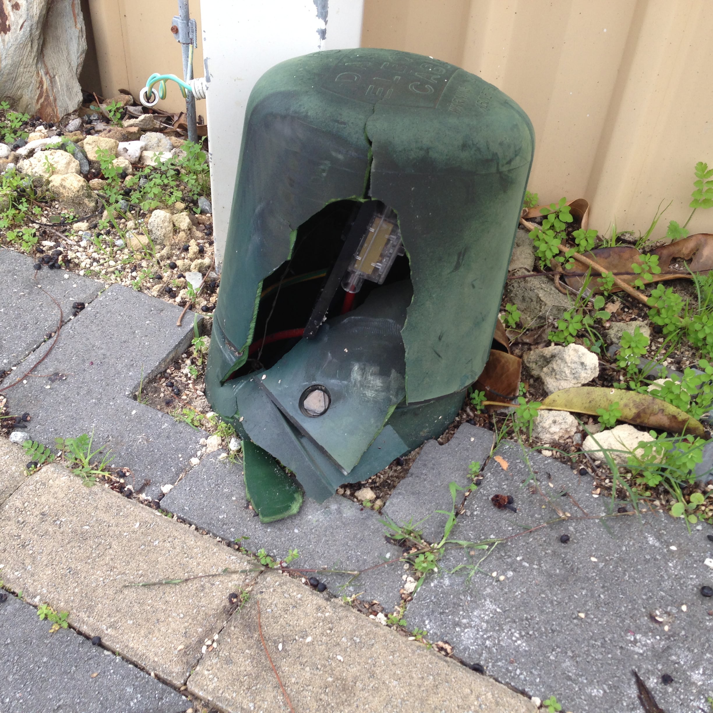 A green dome next to a driveway that is cracked and exposing live electrical cables.