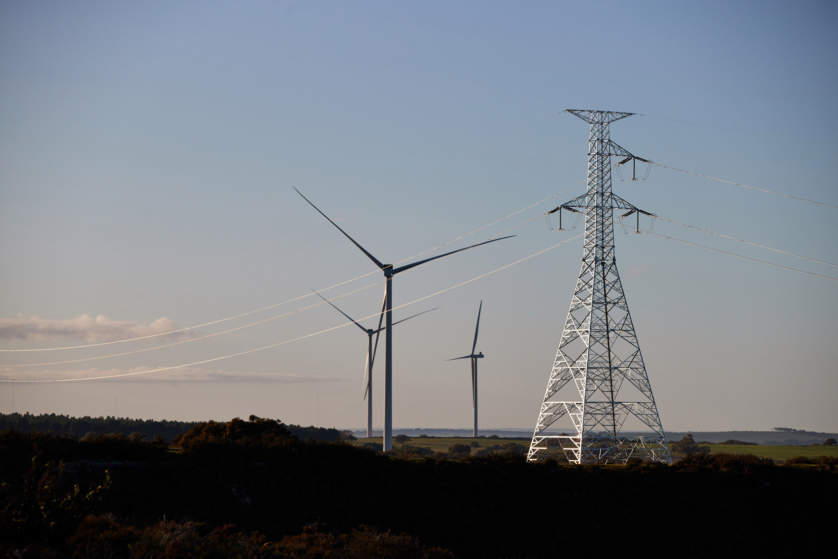 Transmission tower with wind turbines in the background