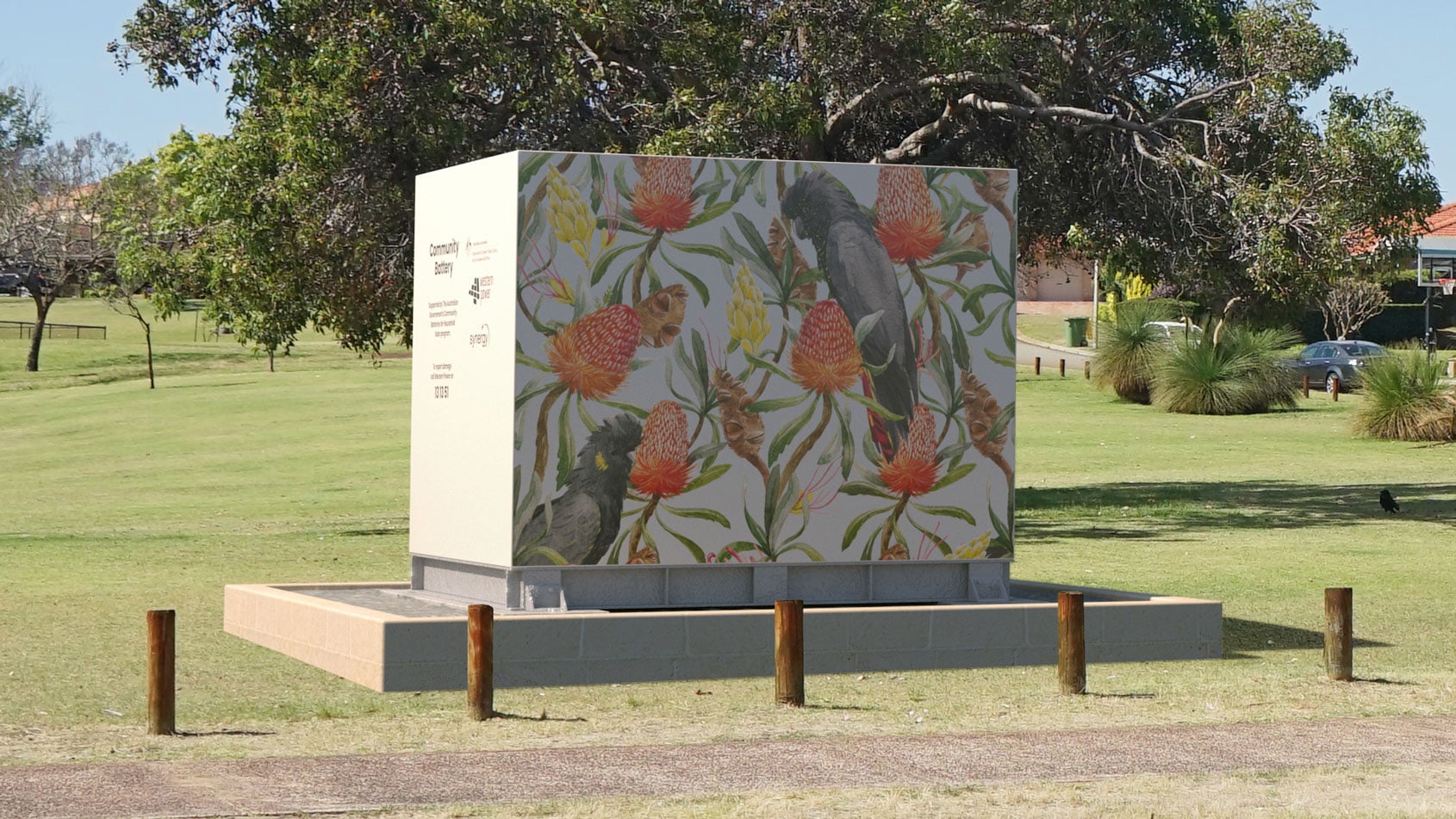 A cube-shaped community battery with bright, colourful decal artwork stands on a raised concrete platform in a grassy park.