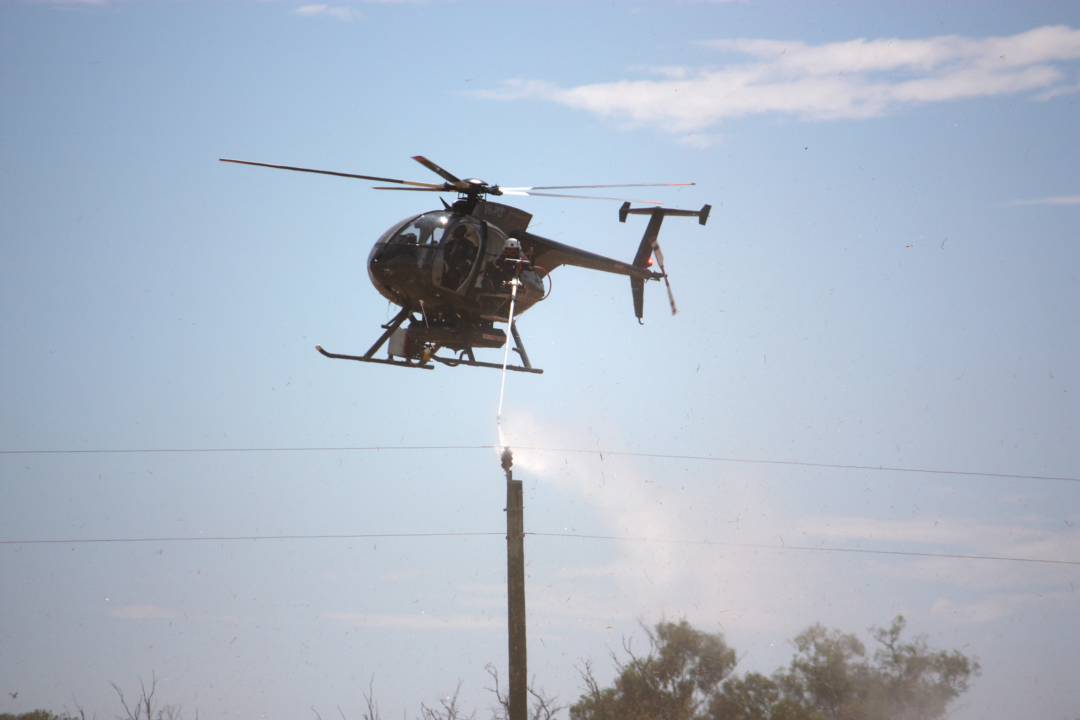 A helicopter washing an insulator on a distribution power pole.