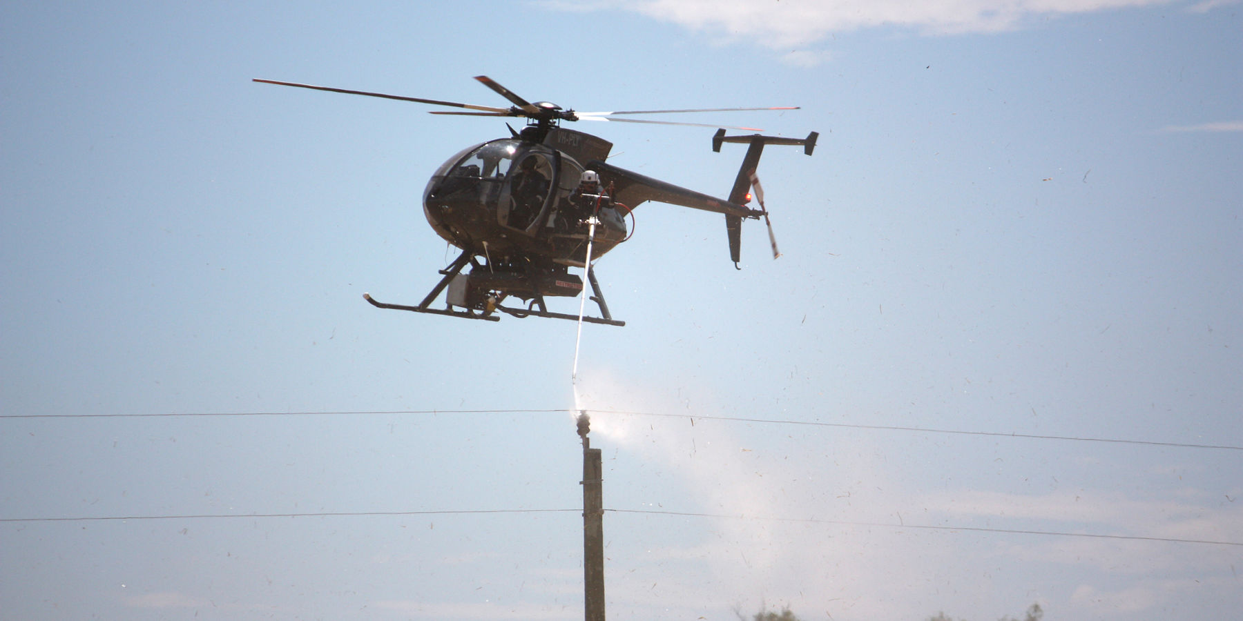 A helicopter washing an insulator on a distribution power pole.